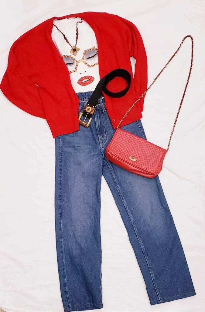 Cardigan rouge porté sur un tee-shirt où l'on voit le visage d'une femme – avec son rouge à lèvres qui donne un bisou. Assorti d'une parie de jeans et d'une sacoche rouge.