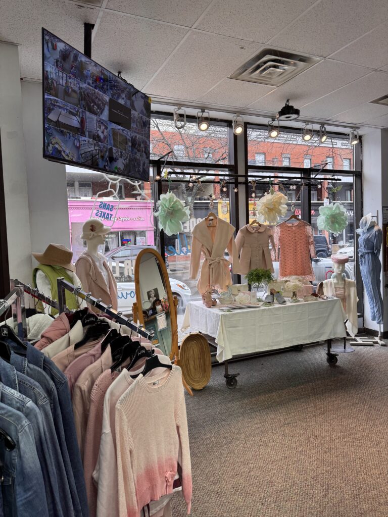 Devanture à Verdun: des couleurs pastel de rose, bleu, vert et crème avec des fleurs en soie et papier énormes. En front d'image on voit des vestes en jeans et des chandails à manches longues en rose